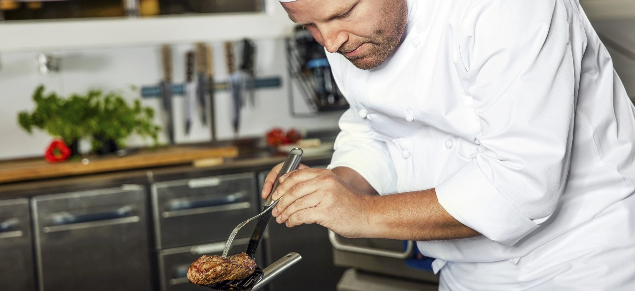 A cook prepares a steak in a commercial kitchen