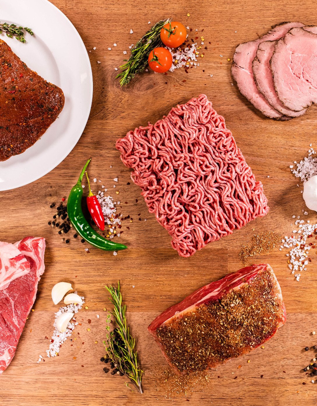 Raw and cooked meat products on a table with a variety of seasonings.