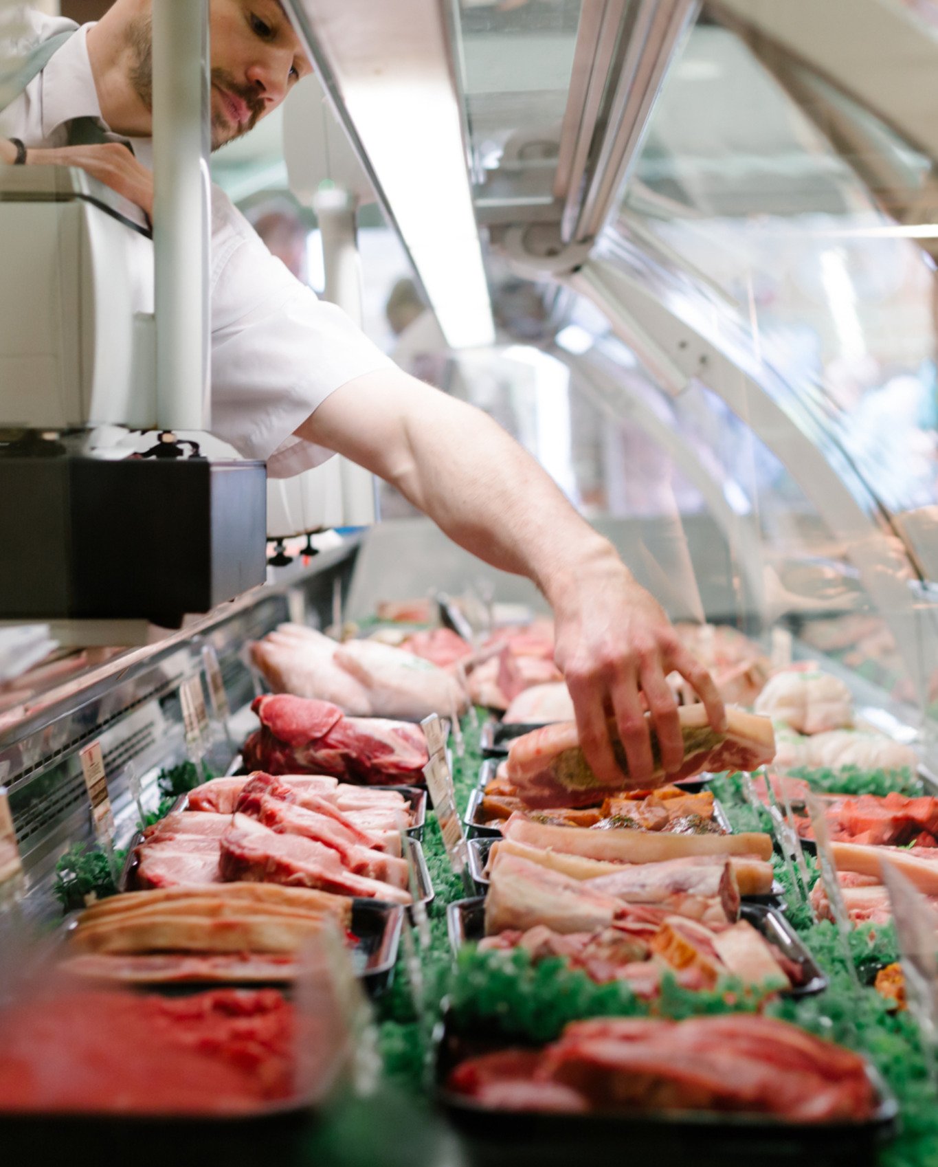 A deli worker arranges deli meats into a display case