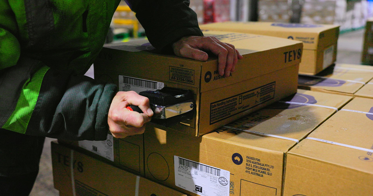 Close-up of Teys export cartons being stamped and sealed in a warehouse, showing Product of Australia labeling and hands-on handling.
